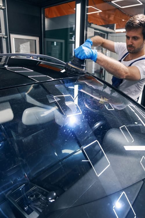 Caucasian automotive repairman with polishing tool grinding the roof of car in workshop