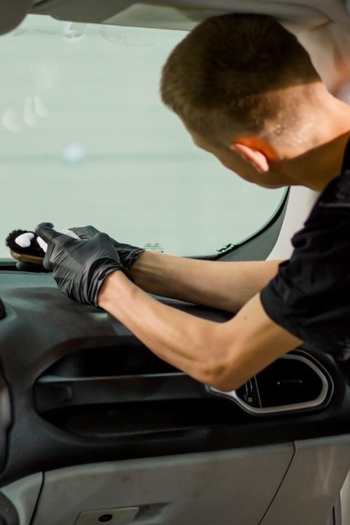 A close-up of a car wash worker using a brush and car chemicals to clean the dashboard of a luxury car during the detailing process