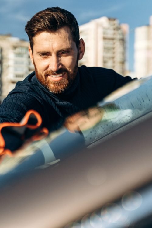 Hand wipe down paint surface of shiny car after polishing. Smiling man cleaning car and drying vehicle with microfiber cloth. Car detailing and car wash concept