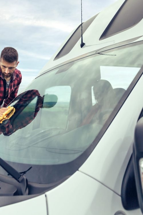 Young man cleaning camper van windshield with cloth outdoor