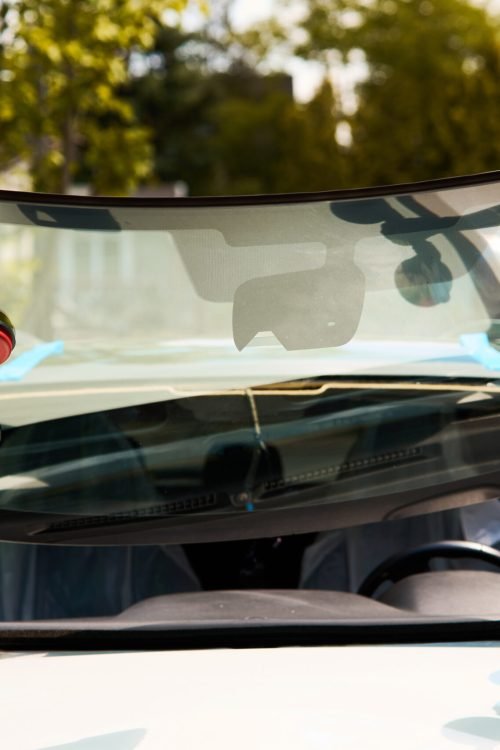 Technicians carry new auto glass towards a car using vacuum lifters during the final stage of an outdoor mobile windshield installation.